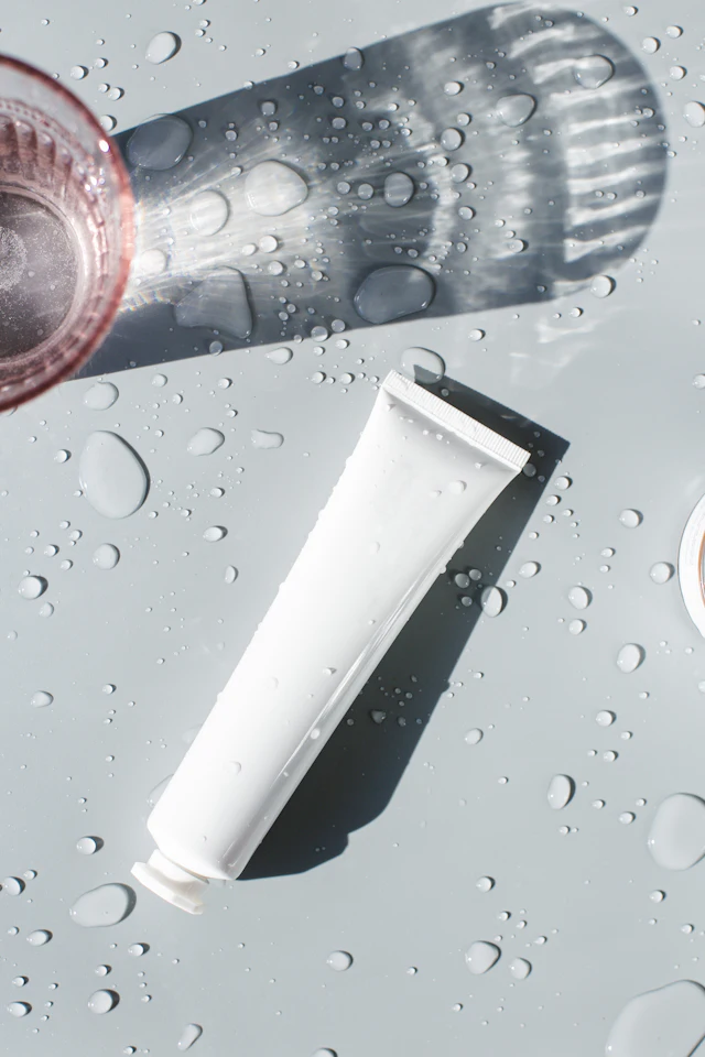 Bisnaga branca de skincare sobre uma superfície com gotas de água